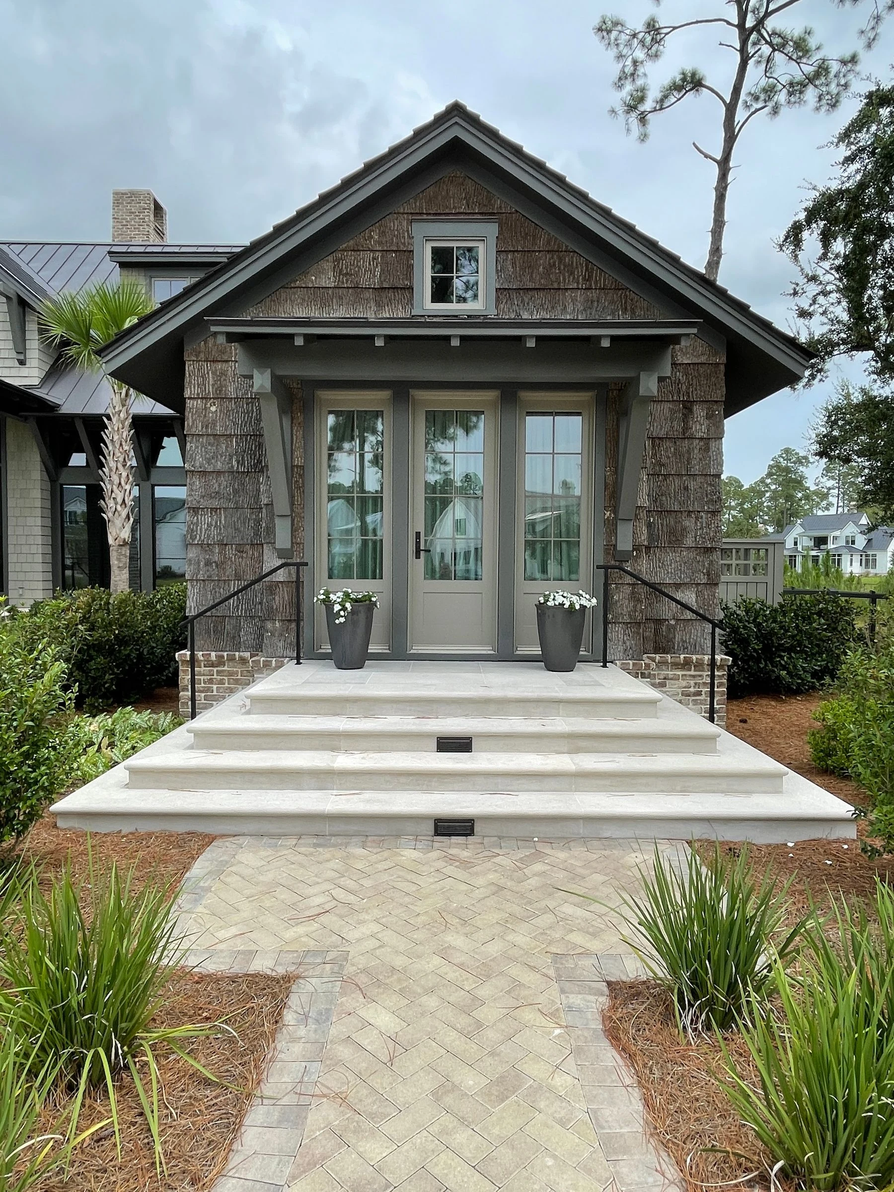 Shingle-clad Bluffton home entrance with French doors, stone steps and matching planters